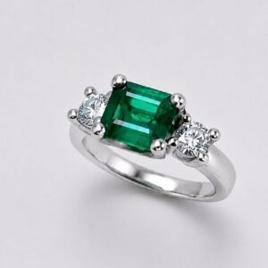 esmeralda y diamantes - Marisa Cano Emerald-cut green emerald ring with two side diamonds on a silver band.