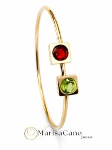 Gold-tone bangle bracelet with two square settings holding a red gemstone on top and a green gemstone below against a white background.